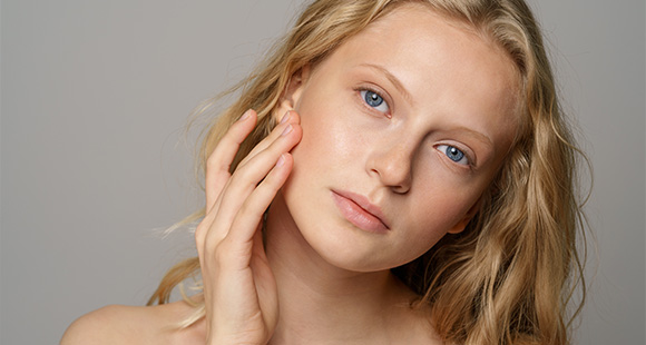 young woman with long wavy hair touching her face showcasing natural beauty and skincare routine